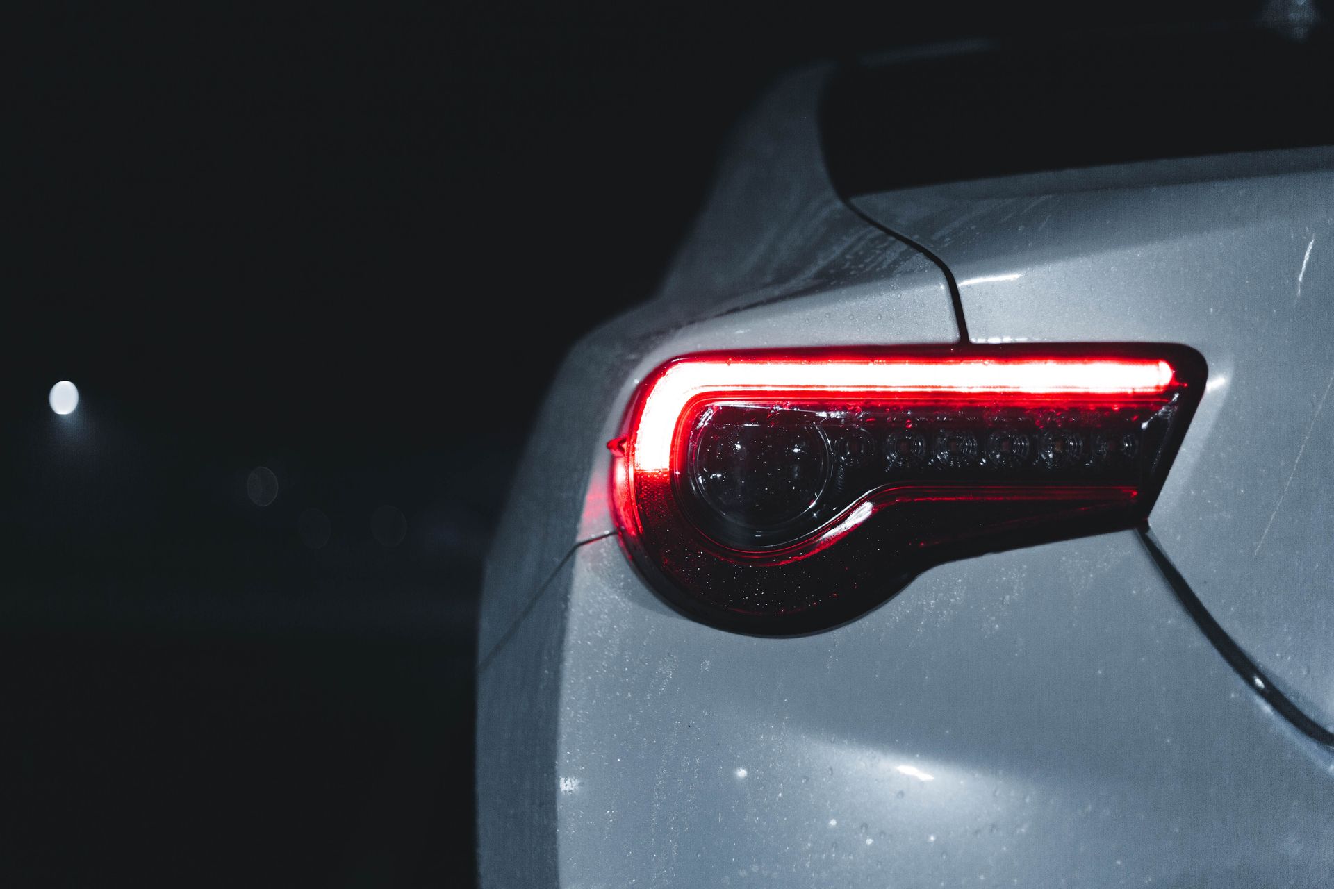 A sleek car's illuminated tail light with water droplets at night, showcasing modern automotive design.